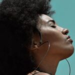 Stylish Fitness - From below side view of young reflective ethnic female model with big earrings and closed eyes under blue sky