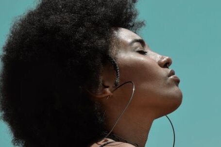 Stylish Fitness - From below side view of young reflective ethnic female model with big earrings and closed eyes under blue sky