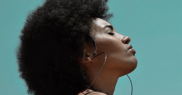 Stylish Fitness - From below side view of young reflective ethnic female model with big earrings and closed eyes under blue sky