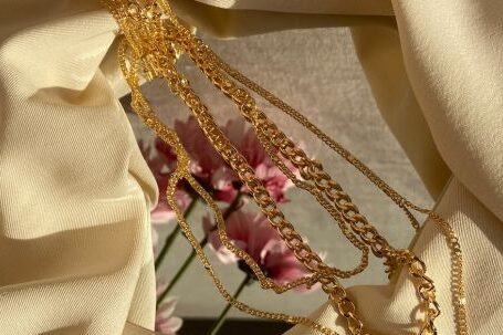 Fashion Inspiration - From above of golden chain with pendant placed on crumpled fabric with mirror near pink flowers in light stylish room