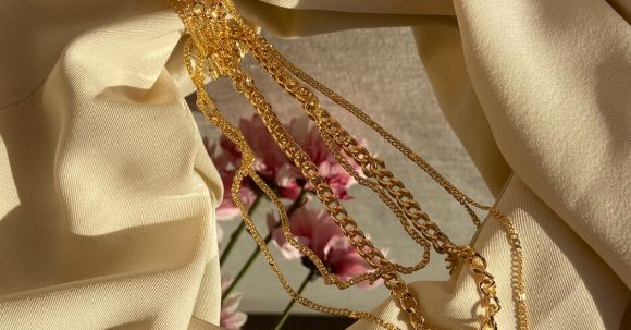 Fashion Inspiration - From above of golden chain with pendant placed on crumpled fabric with mirror near pink flowers in light stylish room