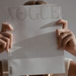 Professional Fashion Tips - Unrecognizable female with big chain on neck standing on white background while covering face with fashion magazine in sunlight
