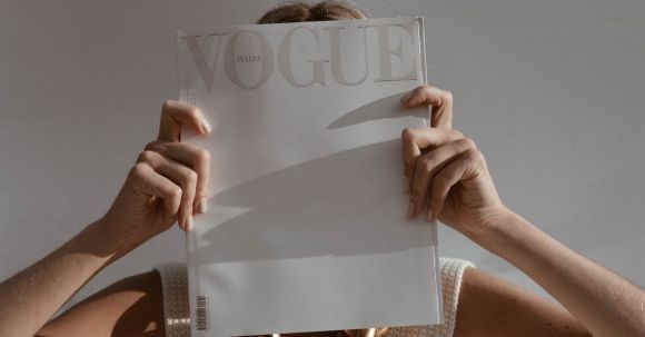 Professional Fashion Tips - Unrecognizable female with big chain on neck standing on white background while covering face with fashion magazine in sunlight