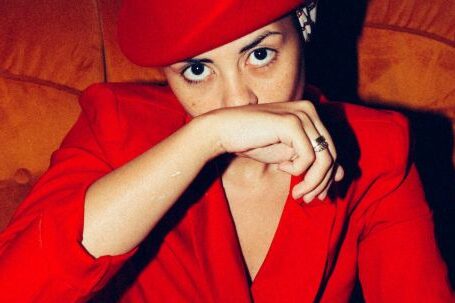 Winter Chic - From above of determined female model wearing trendy suit and retro hat sitting in comfortable armchair and covering mouth with hand while looking at camera